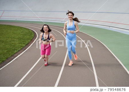 Women in sports outfits jog on running track in city stadium in sunny morning Women in sports outfits jog on running track in city stadium in sunny morning 79548676