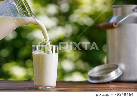 milk pouring from jug into glass outdoors 79549464