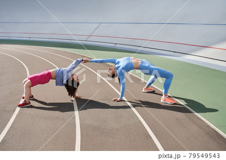 Friends standing in the bridge position and having fun while training at the stadium 79549543