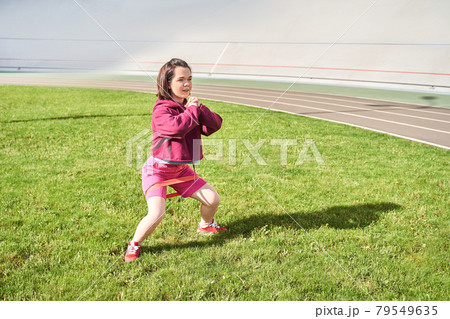 Midget girl with perfect body practicing squats with elastic bands outdoors Midget girl with perfect body practicing squats with elastic bands outdoors 79549635