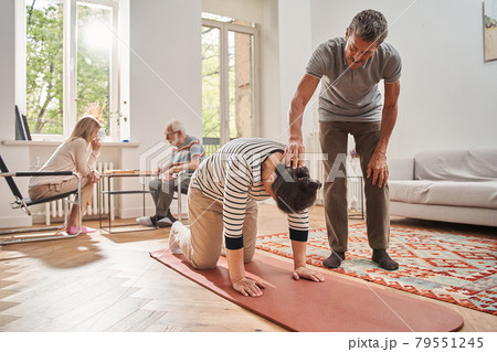 Senior man helping doing morning exercises to his female friend Senior man helping doing morning exercises to his female friend 79551245