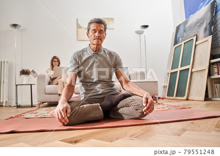 Man in casual clothes meditating and sitting at lotus pose with closed eyes 79551248