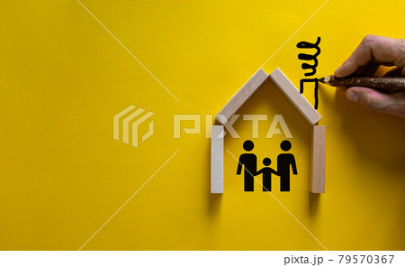 Conceptual image of family values and adoption. House from wooden blocks on beautiful yellow background. Male hand draws with black pencil chimney and smoke. 79570367