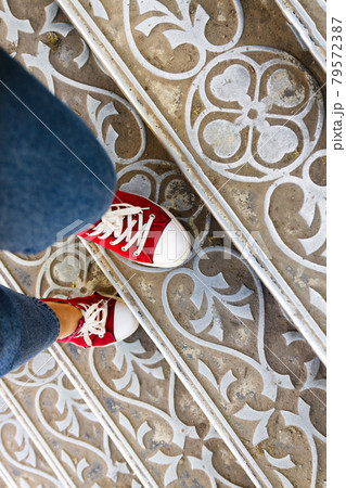 legs in jeans and red sneakers on an antique metal staircase. Top view. 79572387
