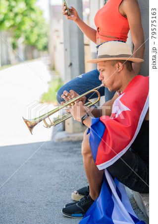 Latino man playing the trumpet next to latina woman checking her phone Latino man playing the trumpet next to latina woman checking her phone 79575163