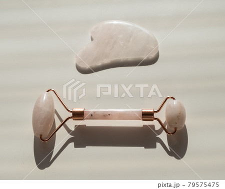 Pink guache scraper and roller on a white table. Equipment for self-massage and skin care for the face and neck Pink guache scraper and roller on a white table. Equipment for self-massage and skin care for the face and neck 79575475