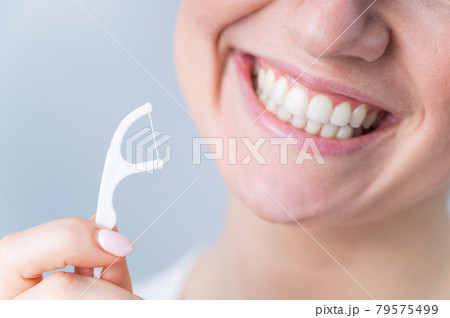 Close-up portrait of a beautiful caucasian woman with a flawless smile holding a toothpick with dental floss on a white background Close-up portrait of a beautiful caucasian woman with a flawless smile holding a toothpick with dental floss on a white background 79575499