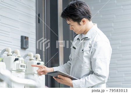 戸建ての玄関前のメーターを点検する若い男性作業員 79583013