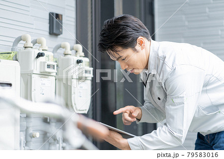 戸建ての玄関前のメーターを点検する若い男性作業員 79583016