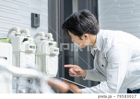 戸建ての玄関前のメーターを点検する若い男性作業員 79583017