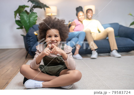Girl showing heart with fingers and parents behind Girl showing heart with fingers and parents behind 79583724