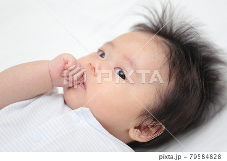 ベッドで寝転んで指しゃぶりをする赤ちゃんの女の子の写真素材