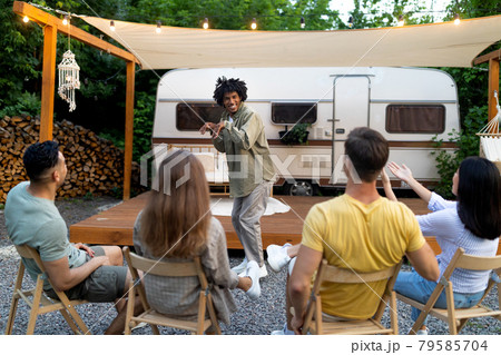 Young multiracial friends playing guess who game, laughing, having fun together near camper van outdoors 79585704