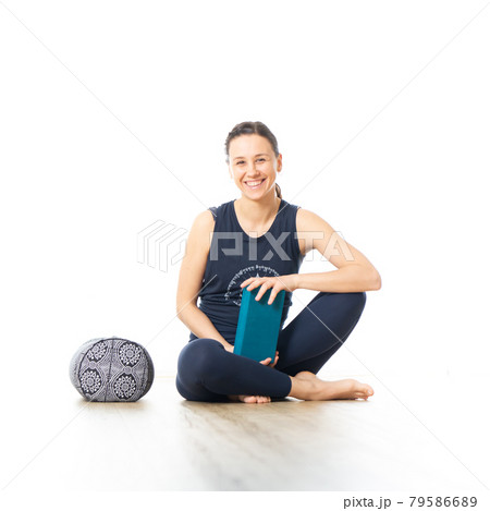 Restorative yoga with a bolster. Young sporty female yoga instructor in bright white yoga studio, smiling cheerfully while preparing restorative yoga exercise props Restorative yoga with a bolster. Young sporty female yoga instructor in bright white yoga studio, smiling cheerfully while preparing restorative yoga exercise props 79586689