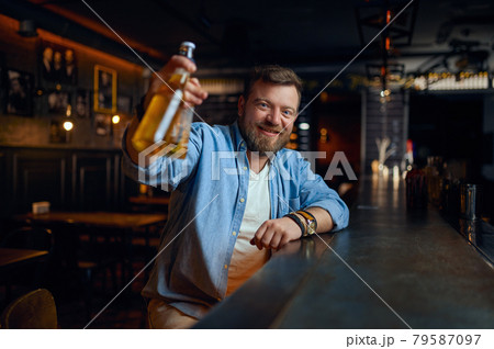 Smiling man with bottle of beer at counter in bar Smiling man with bottle of beer at counter in bar 79587097
