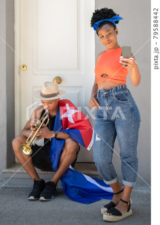 Latina woman taking a photo of herself next to a latino man with a cuban flag playing a trumpet 79588442