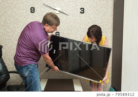 A man and a woman bring a new TV into the apartment 79589312