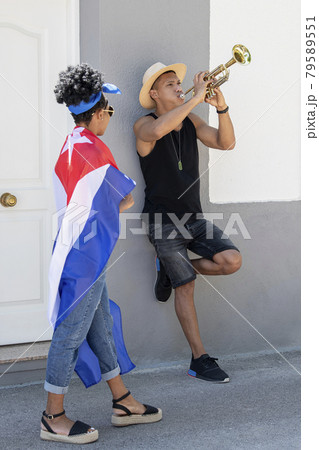 Curious latina woman observing a latino man playing the trumpet: Selective focus. Art and diversity concept. 79589551