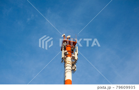A white and red tower with cellular communication antennas on a sky 79609935