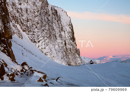 Majestic winter landscape with a snowmobile riding near a high rocky cape. Majestic winter landscape with a snowmobile riding near a high rocky cape. 79609969