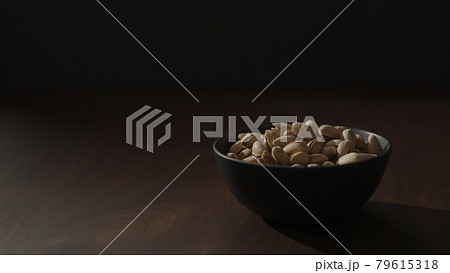 Slow motion handheld shot of roasted pistachios in black bowl on walnut table 79615318