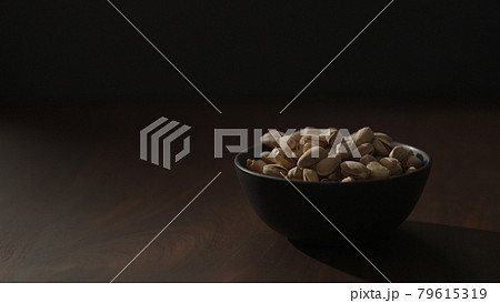 Slow motion handheld shot of roasted pistachios in black bowl on walnut table 79615319