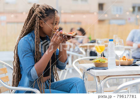 Cute afro american woman enjoying a pizza slice and rinks at an outdoors terrace 79617781