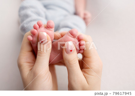 Feet of the newborn in the hands of the mother. Mother holds baby's feet. Feet of the newborn in the hands of the mother. Mother holds baby's feet. 79617945