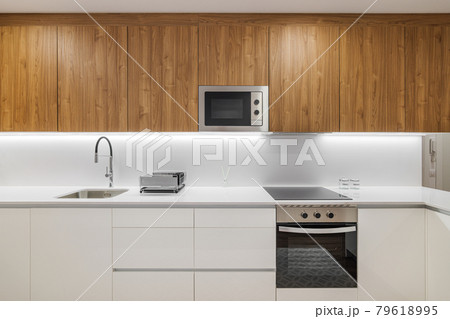 Stylish kitchen with modern furniture in white color with wooden cupboards for kitchenware. Contemporary style interior after home renovation 79618995
