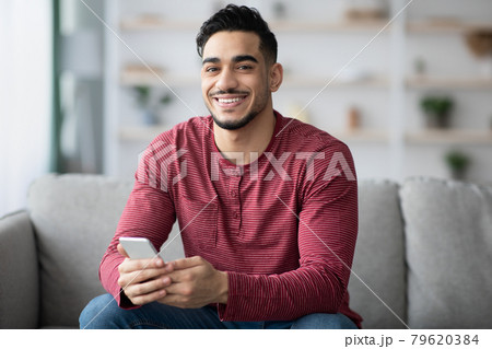Positive arab guy using brand new cellphone, home interior 79620384