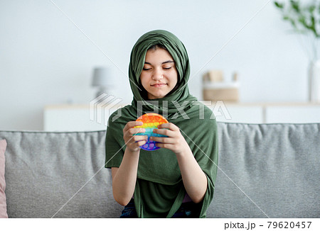 Portrait of lovely Indian teen girl in hijab playing with bright POP IT toy, enjoying fun antistress game at home 79620457
