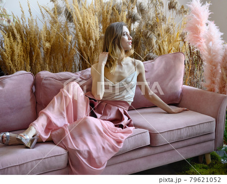 Young adult woman sitting on a sofa in a room in tall grass Young adult woman sitting on a sofa in a room in tall grass 79621052