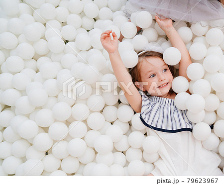 cheerful little girl in a dry pool with white balls. playground. 79623967