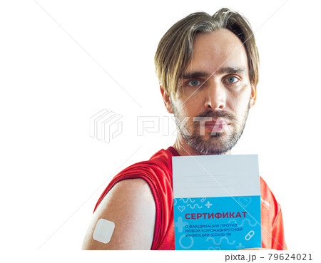 A man with a beard after being vaccinated against coronavirus with a patch pasted on his shoulder holds a vaccination certificate in his hand 79624021