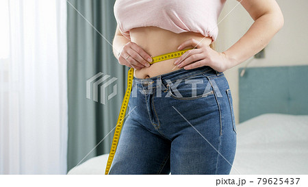 Beautiful slim woman measuring her waistline with yellow measuring tape. Concept of dieting, loosing weight and healthy lifestyle. Beautiful slim woman measuring her waistline with yellow measuring tape. Concept of dieting, loosing weight and healthy lifestyle. 79625437