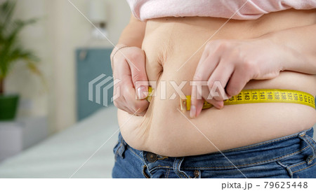 Young woman suffering from excess weight measuring her big belly. Concept of dieting, unhealthy lifestyle, overweight and obesity 79625448
