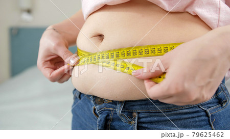 CLoseup of woman measuring her big fat stomach at mirror. Concept of dieting, unhealthy lifestyle, overweight and obesity CLoseup of woman measuring her big fat stomach at mirror. Concept of dieting, unhealthy lifestyle, overweight and obesity 79625462