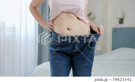 Beautiful slim woman wearing her old jeans that are big for her. Concept of dieting, loosing weight and healthy lifestyle. 79625542