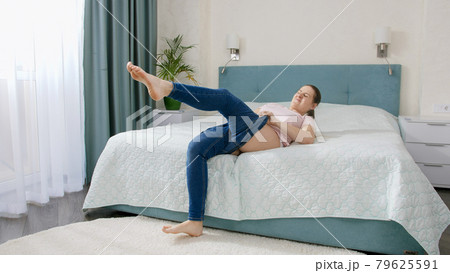 Young woman dressing up and fitting tight jeans in bedroom at morning. Young woman dressing up and fitting tight jeans in bedroom at morning. 79625591