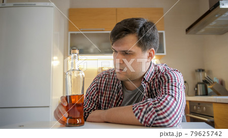 Young woman taking bottle of alcohol during conflict with drunk husband on kitchen. Alcoholism and addiction problems Young woman taking bottle of alcohol during conflict with drunk husband on kitchen. Alcoholism and addiction problems 79625742