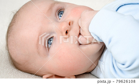 Portrait of cute little baby boy holding hand in mouth. Concept of children development and family lifestyle Portrait of cute little baby boy holding hand in mouth. Concept of children development and family lifestyle 79626108
