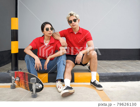 Asian couple resting after skateboarding. Young man in red T-shirt with collar and black sunglasses rest his arm at his girlfriend's shoulder. 79626130