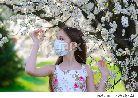 Lonely teenage girl wearing protection medicine mask against virus and allergy enjoying spring flower blossom in blooming garden 79626722
