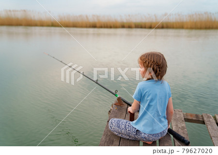 little girl sits on a wooden bridge on a river with fishing rod. little girl sits on a wooden bridge on a river with fishing rod. 79627020