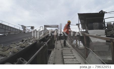 Male worker in respirator looking at conveyor belt with stones 79632051