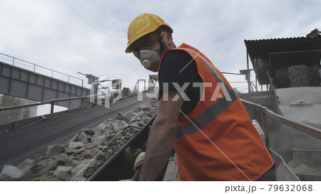 Male worker in respirator looking at conveyor belt with stones 79632068