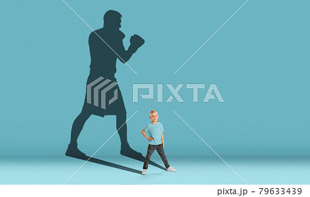 Childhood and dream about big and famous future. Conceptual image with boy and shadow of strong male boxer on blue background. Dreams, imagination, education concept. 79633439