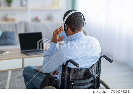 Back view of paraplegic black guy in wheelchair wearing headphones, using laptop with mockup for design at home Back view of paraplegic black guy in wheelchair wearing headphones, using laptop with mockup for design at home 79637821