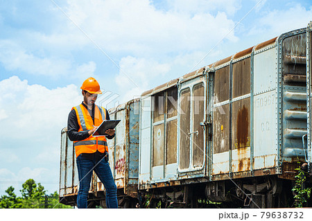 Inspector Engineering wearing helmet and vest worker unifrom checking railway construction work on rail track. Asian workers and coworkers stand beside old train bogies. 79638732