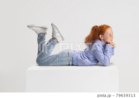 Side view. Portrait of smiling red-headed girl in casual clothes isolated on white studio background. Happy childhood concept. Sunny child. Looks happy, delighted 79639313